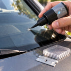 Hand holding the Chipmend resin bottle with its nozzle at a small chip on a windshield, film squares and blade on the hood